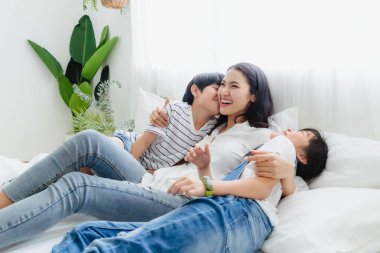 Güzel, mutlu, Asyalı bir aile sıcak bir evde. Oğlan ve kız, anneyi zevkle öperler, rahatlar ve yatak odasında birlikte oynarlar. Mutluluk ilişkisi ve ebeveynler ve çocuklar arasında sevgi bağı.