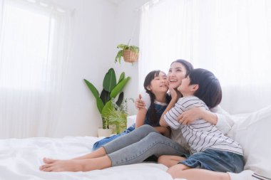 Güzel, mutlu, Asyalı bir aile sıcak bir evde. Oğlan ve kız, anneyi zevkle öperler, rahatlar ve yatak odasında birlikte oynarlar. Mutluluk ilişkisi ve ebeveynler ve çocuklar arasında sevgi bağı.