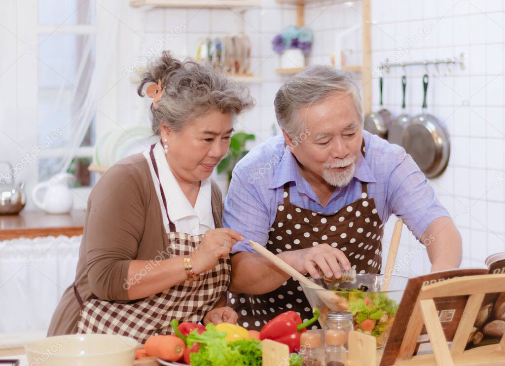Happy & smiling attractive elderly cute Asian couple in love enjoying cooking healthy salad in kitchen at home together. Happiness family of beautiful romantic married lover or marriage relationship