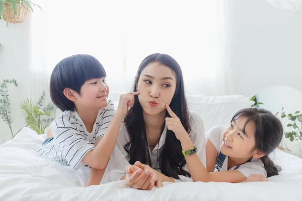 Güzel, mutlu, Asyalı bir aile sıcak bir evde. Gülümseyen anne, oğul ve kız yatak odasında eğleniyor, rahatlıyor ve oyun oynuyorlar. Mutluluk ilişkisi ve ebeveynler ve çocuklar arasındaki sevgi bağı anı