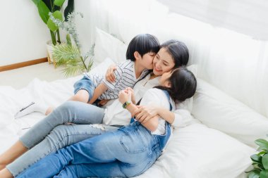 Güzel, mutlu, Asyalı bir aile sıcak bir evde. Oğlan ve kız, anneyi zevkle öperler, rahatlar ve yatak odasında birlikte oynarlar. Mutluluk ilişkisi ve ebeveynler ve çocuklar arasında sevgi bağı.