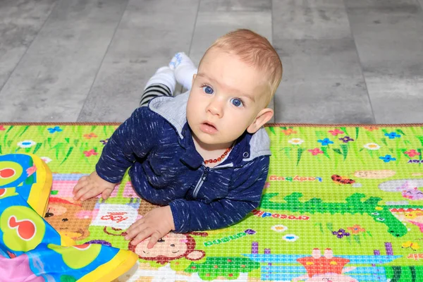 Nahaufnahme eines glücklichen neun Monate alten Jungen, der auf einer bunten Spielmatte krabbelt. ein neun Monate alter Junge mit blonden Haaren und blauen Augen. — Stockfoto