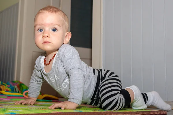 Ein neun Monate alter Junge mit blonden Haaren und blauen Augen. Junge spielt auf dem Boden. Baby posiert für einen Fotografen — Stockfoto