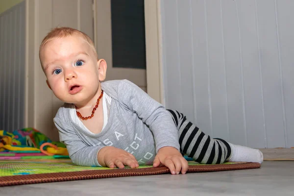 Das süße Baby liegt auf dem Boden und blickt in die Kamera. ein neun Monate alter Junge mit blonden Haaren und blauen Augen. — Stockfoto