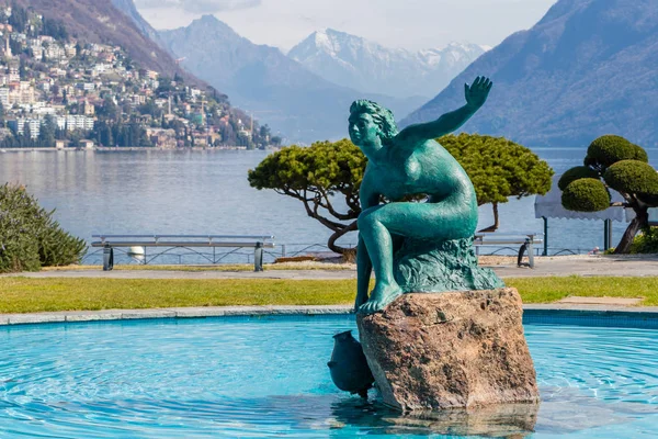 Lugano Gölü 'nün yanında İsviçre' nin İtalyan bölgesinde mavi suyun ortasında güzel bir heykel bulunan bir çeşme.