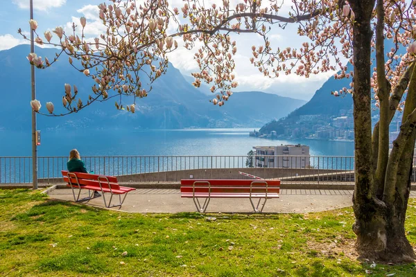 Girl enjoying city view from a bench under the Magnolia tree at the hill in Lugano, view at the Lake Lugano and Alps mountains in Ticino canton of Switzerland — Stock Photo, Image