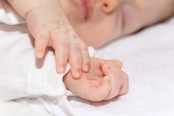 Uyurken yatakta uzanan huzurlu bir bebek. Bebek 2 aylık, yakın plan ve bebek ellerine odaklanıyor.