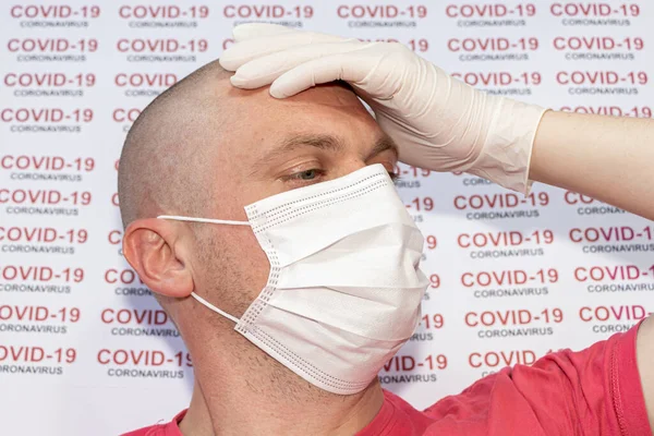 Sad sick man holds his hand on his forehead with a worried expression on his face. A man wearing medical mask and gloves with COVID-19 coronavirus text at white background.