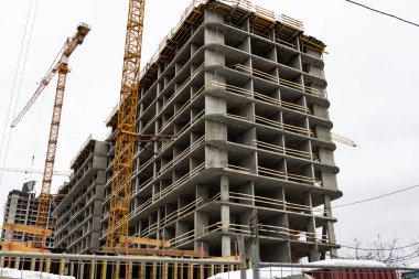 Gri gökyüzüne karşı vinçle güçlendirilmiş beton çerçeveden yapılmış bir inşaat alanında.