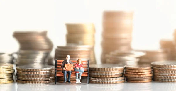 Miniature people: Elderly people sitting on coins stack. Retirement planning. money saving and Investment. Time counting down for retirement and pension.