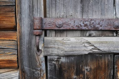 Pasla kaplı eski bir demir kapı menteşesi eski bir ahşap kapıya asılı.