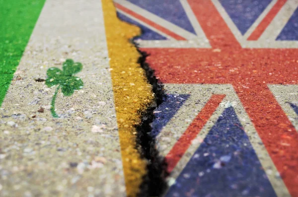 Flags of Great Britain and Ireland on asphalt are separated by a crack.