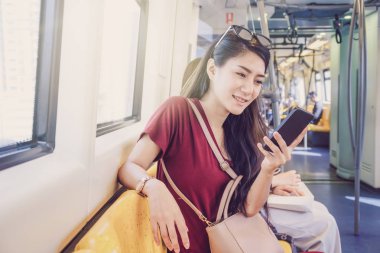 Asyalı kadın yolcu seyahat büyük şehirde Bts Skytrain raylar veya Mrt metro akıllı cep telefonu üzerinden sosyal ağ kullanarak rahat takım elbise ile