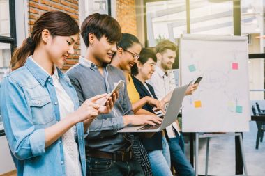 Asya grup ve çok ırklı iş insanlarla rahat takım mobil teknolojisiyle, tablet, dizüstü bilgisayar ve bilgisayar modern ofis çalışma veya sosyal ağ için