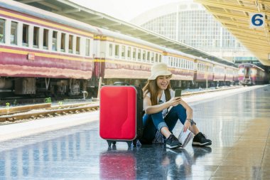 Asya kadın oturuyor ve akıllı cep telefonu önce bakarak Traveller tren istasyonu, seyahat ve yaşam tarzı kavramı seyahat gitmek