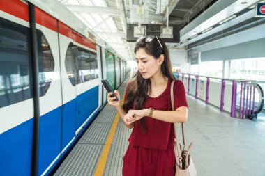 Asyalı kadın yolcu saat izliyor ve Bts Skytrain raylar veya Mrt metro seyahat büyük şehir, yaşam tarzı ve ulaşım konsepti için bekliyor casual elbise ile