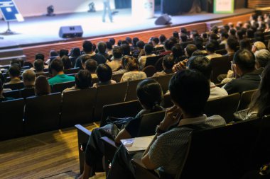 Konferans salonu veya seminer toplantı ile düşük ışık durum, iş ve eğitim yatırım kavramı hakkında sahnede hoparlörleri dinleme seyirci arkadan görünüş