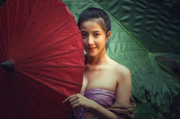 Closeup Portrait of beautiful Village women standing with red color traditional umbrell in forest, countryside and Folkways concept