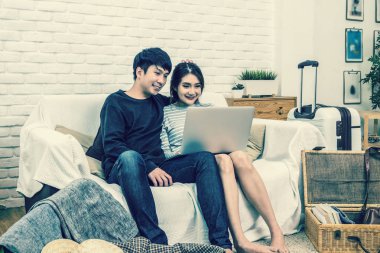 Mutlu Asya çift planlama ve modern evde oturma odası, çift, yaşam tarzı ve gezgin kavramı kanepede teknoloji dizüstü bilgisayar ile seyahat için otel rezervasyonu,