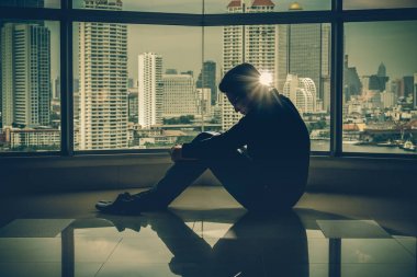 Cityscape arka plan üzerinde dramatik kavramı üzerinde windows yanında düşük ışık çevre ile iç gökdelenler depresif adam kafa otururken eller