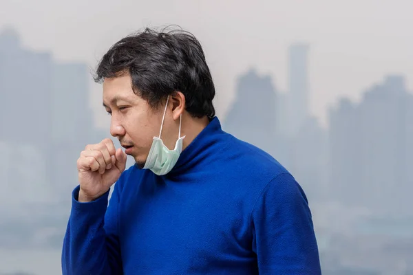バンコクの街並み背景 ヘルスケアの概念上の汚染と重い霧を見ることができる高いアパートのバルコニーで咳を大気汚染に対して顔のマスクを身に着けているアジア人男性 — ストック写真