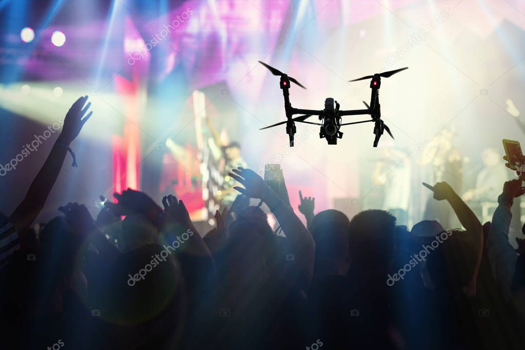 Closeup silhouette of Drone flying for taking video of Concert crowd and Music fanclub with show hand action which follow up the songer at the front of stage, musical and concert concept