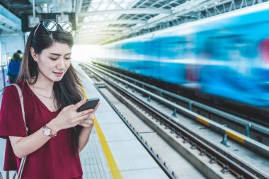 Asyalı kadın yolcu seyahat büyük şehir, yaşam tarzı ve ulaşım kavramında sosyal ağ üzerinden Bts Skytrain raylar veya Mrt metro akıllı cep telefonu kullanarak rahat takım elbise ile