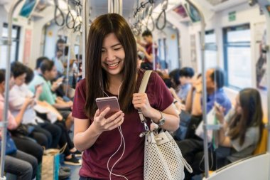Asyalı kadın yolcu seyahat büyük şehir, yaşam tarzı ve ulaşım kavramında Skytrain raylar veya metro akıllı cep telefonu kullanarak rahat takım elbise ile