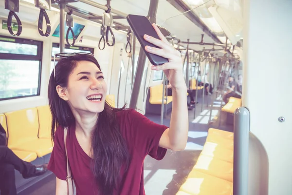 亚洲女乘客与休闲服采取自拍的智能手机在 Bts 轻轨铁路或捷运地铁在大城市的旅行 生活方式和交通概念 — 图库照片