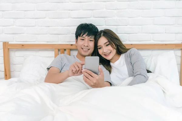 Glückliche Asiatische Paar Mit Der Technologie Smartphone Auf Dem Bett — Stockfoto