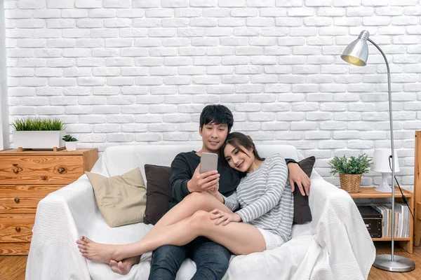 Mutlu Asya çift oturma ve modern ev, çift başarılı ve yaşam tarzı concept, oturma odası kanepe üzerinde dijital akıllı cep telefonu için selfie kullanma