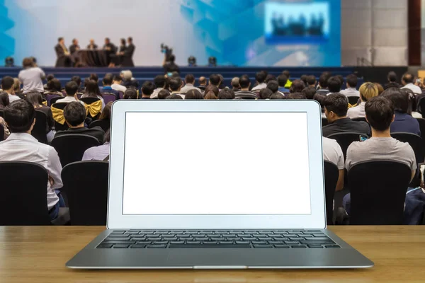 在木桌上的膝上型计算机在会议厅或研讨会会议上的观众观看演讲嘉宾在舞台 商业技术和教育理念方面的发言者 — 图库照片