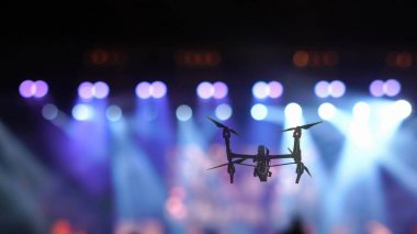 Konser kalabalığının videosu için uçan Drone 'un yakın çekim silueti ve konferans salonundaki spot ışıklarının bulanık fotoğrafı, müzikal ve konser konsepti