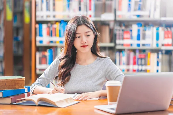 カジュアルなスーツを着たアジアの若い学生は 宿題をしたり 大学の図書館でテクノロジーラップトップを使用したり 本棚の背景の上に様々な本や文房具を持つコラージュを使用して 学校に戻ります — ストック写真