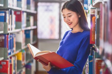 Sıradan takım elbiseli Asyalı genç Öğrenci ayakta ve üniversite kütüphanesi veya çeşitli kitap arka plan ile kolaj kitap rafında kitap okuma, Okula dönüş kavramı