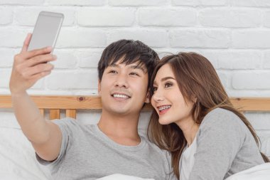 Mutlu Asya oturma ve yatak odası modern evde, yatakta selfie için dijital akıllı cep telefonu kullanarak aşık çift başarılı ve yaşam tarzı kavramı