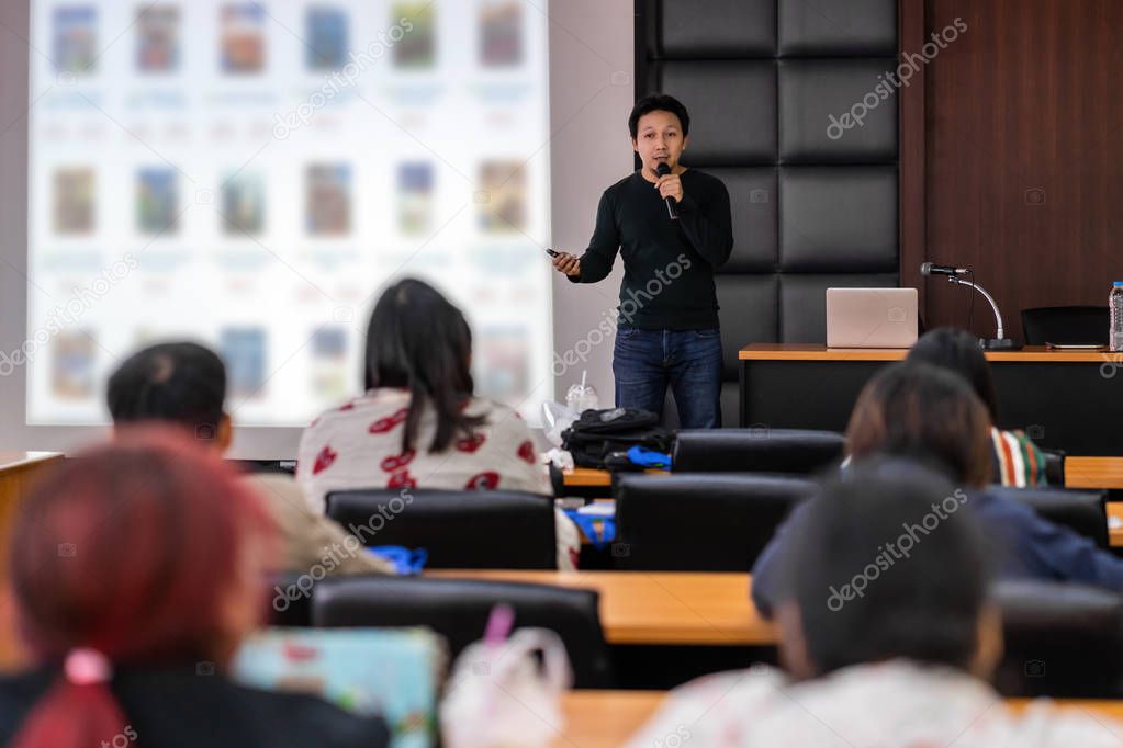 Asian Speaker or lecture with casual suit on the stage presenting via projector screen in the conference hall or seminar meeting room to Audience, business education and Seminar concept