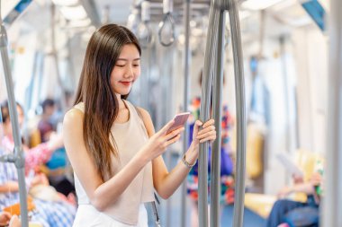 Genç Asyalı kadın yolcu metroda seyahat ederken, metroda, Japonca, Çince, Kore yaşam tarzı ve günlük yaşamında, banliyö ve ulaşım kavramında sosyal ağı akıllı cep telefonuyla kullanıyor.