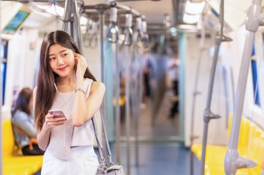 Genç Asyalı kadın yolcu metroda, Japonca, Çince, Kore yaşam tarzı ve günlük yaşam, banliyö ve ulaşım kavramında seyahat ederken akıllı cep telefonuyla müzik dinliyor.