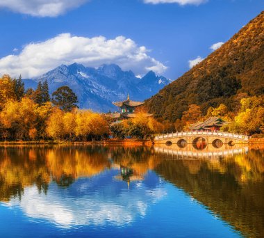 Jade Spring Park 'taki Kara Ejder Havuzu' nun mavi gökyüzünün altındaki Yeşim Ejder Dağı üzerindeki mermer köprüyle manzarası, Lijiang, Yunnan, Çin. Çin kültürü ve seyahat kavramı