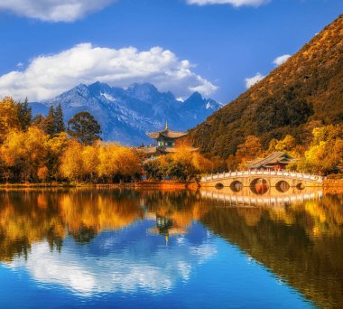 Landscape view of the Black Dragon Pool at Jade Spring Park with marble bridge over the Jade dragon mountain under blue sky, Lijiang, Yunnan province, China. China culture and travel concept clipart