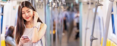 Banner, web sayfası ya da metro istasyonunda, Japon, Çinli, Koreli yaşam tarzı, boş zaman ve günlük yaşam tarzında akıllı cep telefonuyla müzik kullanan ve dinleyen genç Asyalı kadın yolcu şablonu, 