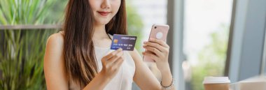 Genç Asyalı bir kadın kahve dükkanında online alışveriş için cep telefonu kullanıyor ya da pencere aynası, teknoloji para cüzdanı ve online ödeme konsepti, kredi kartı modeli