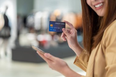 Online mağazada elbise dükkanı mağaza arka plan, teknoloji para cüzdanı ve online ödeme kavramı, kredi kartı mockup alışveriş için cep telefonu ile kredi kartı ile portre Asyalı kadın