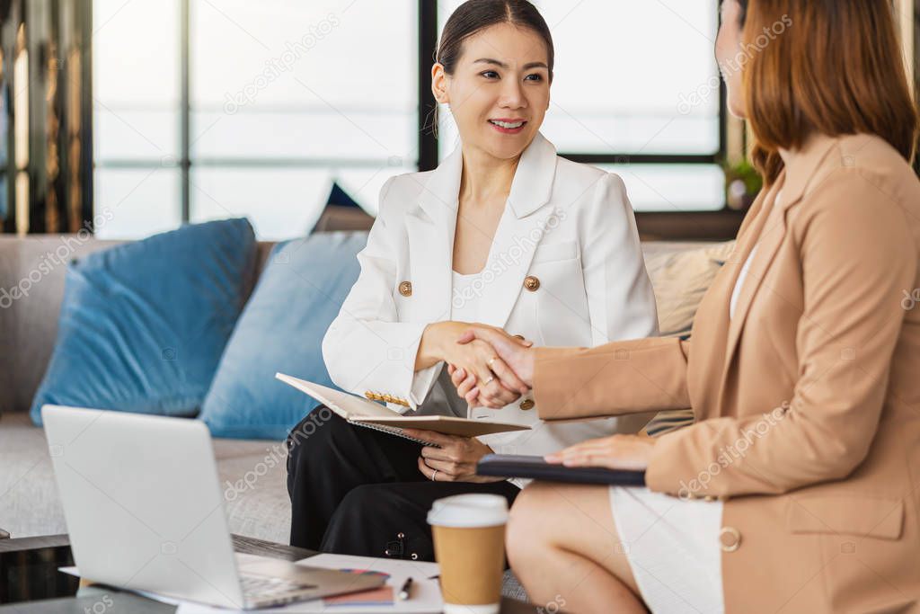 Two asian businesswomen happiness Reach an agreement by shaking hand together after successful deal the business contract in modern office or coworking space, success partnership concept