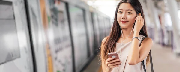 Banner, web page or cover template of Young Asian woman passenger using and listening music via smart mobile phone in subway train station, japanese,chinese,Korean lifestyle, leisure and daily life,