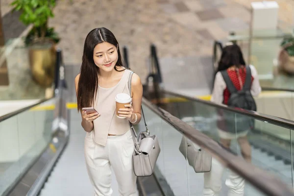日本語 中国語 韓国語の生活や日常生活 通勤や交通機関で旅行するときに スマートフォンを使用してデパートでエスカレーターを歩く若いアジアの女性の乗客 — ストック写真