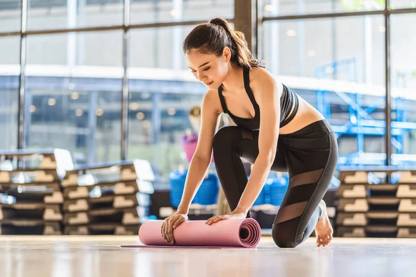 アジアの若い女性は ヨガスポーツの前と後にヨガマットを転がし 展開し 健康や瞑想の練習のために準備し スポーツウェアのブラジャーとパンツ スポーツや医療の概念を身に着けています — ストック写真