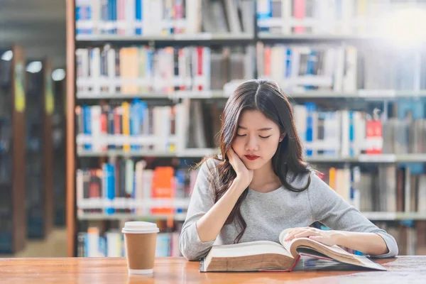 本の棚の上に木製のテーブルの上に大学や大学の図書館でコーヒーのカップで本を読んでカジュアルなスーツでアジアの若い学生 学校の概念に戻る — ストック写真