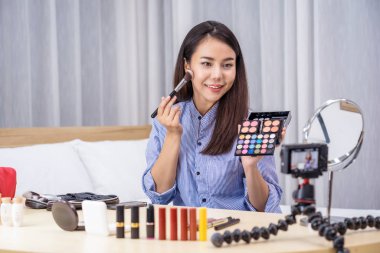 Çekici Asyalı kadın güzellik blogcusu veya vlogger palet ile makyaj yapıyor ve sosyal ağ medyasında video veya cep telefonuyla yaşıyor, video kaydı, makyaj dersi, kozmetik vlog konsepti